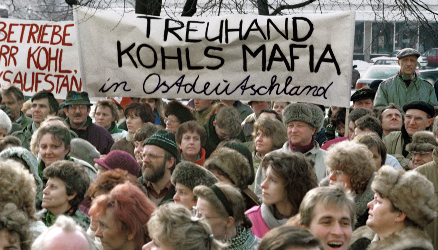 Bei einer Demonstration gegen die Treuhandanstalt im Jahre 1991 am Alexanderplatz in Berlin halten Teilnehmer ein Transparent mit der AUfschrift: Treuhand Kohls Mafia in Ostdeutschland © dpa/Paul Glaser Bei einer Demonstration gegen die Treuhandanstalt im Jahre 1991 am Alexanderplatz in Berlin halten Teilnehmer ein Transparent mit der AUfschrift: Treuhand Kohls Mafia in Ostdeutschland © dpa/Paul Glaser