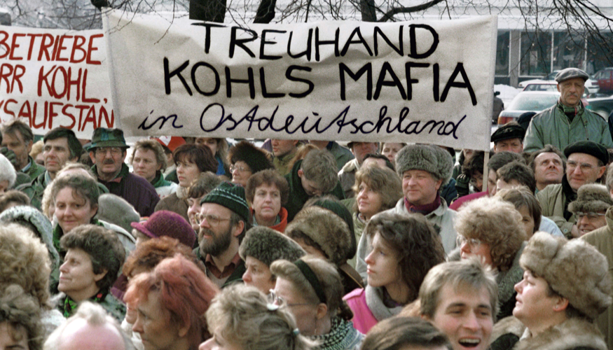 Bei einer Demonstration gegen die Treuhandanstalt im Jahre 1991 am Alexanderplatz in Berlin halten Teilnehmer ein Transparent mit der AUfschrift: Treuhand Kohls Mafia in Ostdeutschland © dpa/Paul Glaser